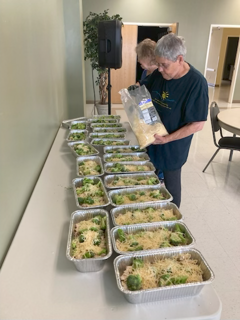 Spark volunteers placing the cheese layer on a family style meal